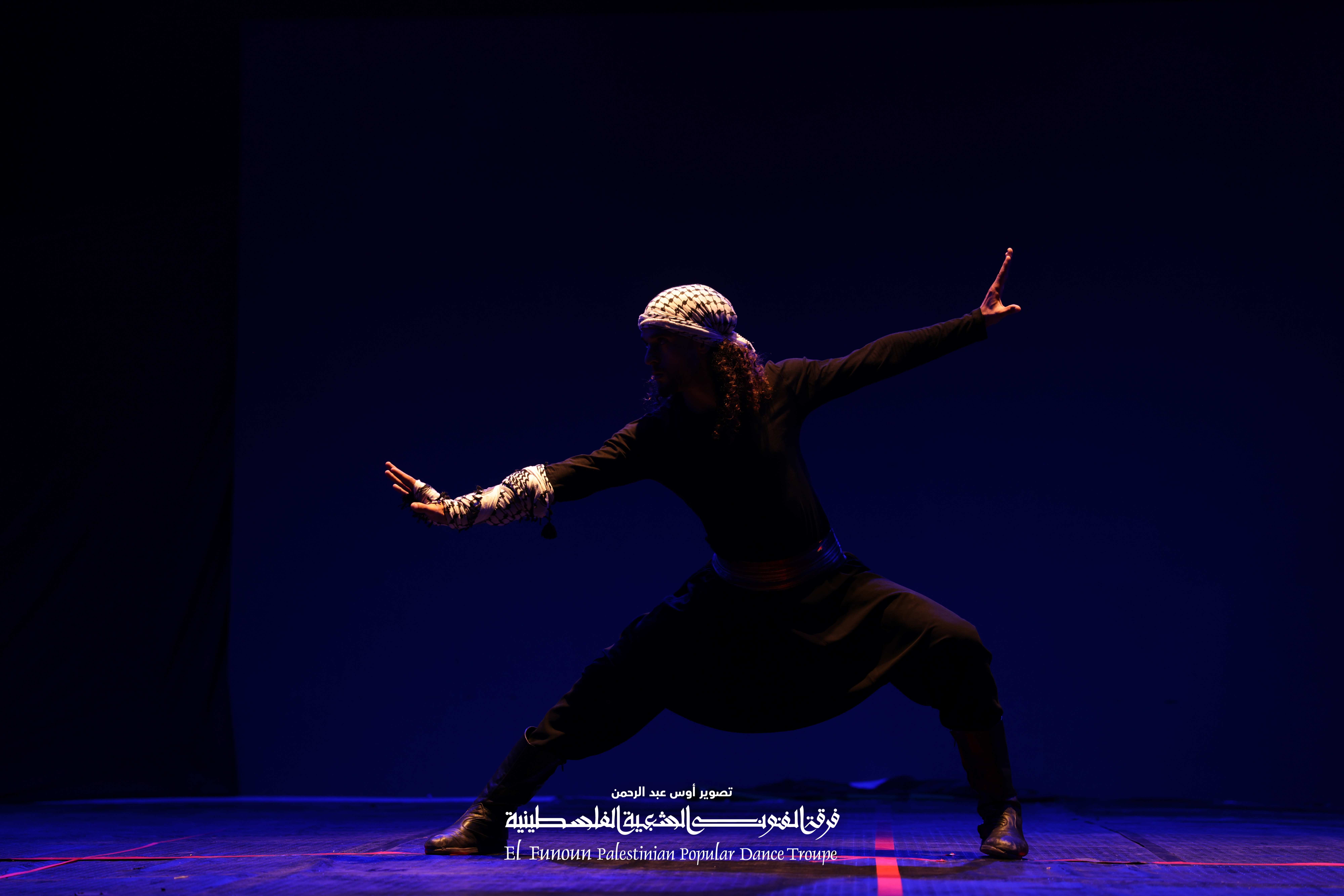 Dancer performing with El-Funoun Palestinian Popular Dance Troupe, wearing traditional keffiyeh with arms outstretched