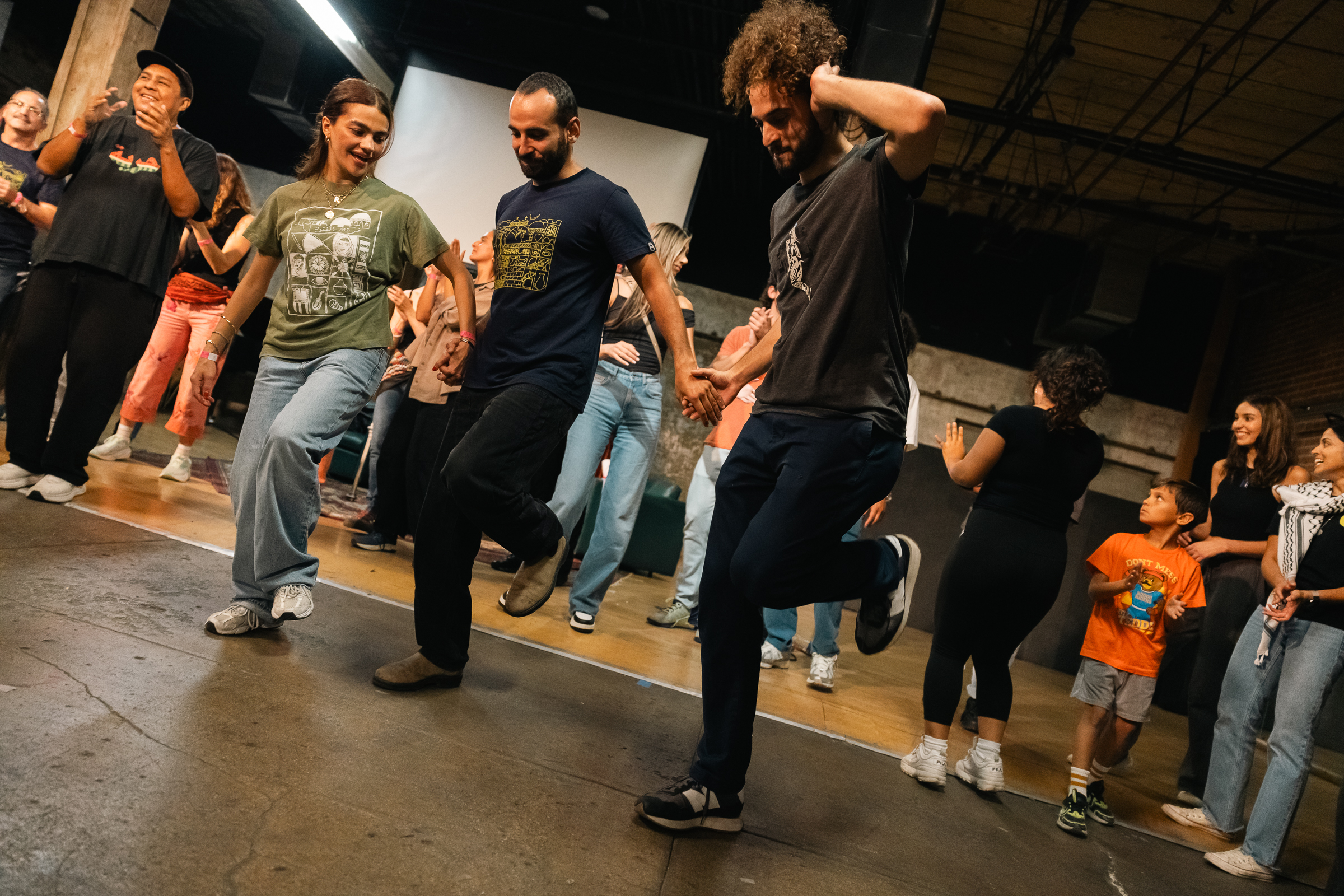 Three dancers performing dabke in studio with audience watching