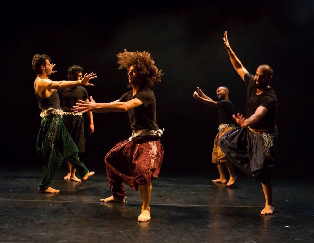 The Rooster performance - five male dancers in black shirts and colorful harem pants performing expressive contemporary dance movements on stage