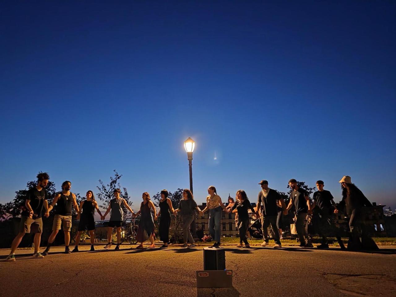 Street Dabka workshop in New York - people holding hands in a line dancing at dusk